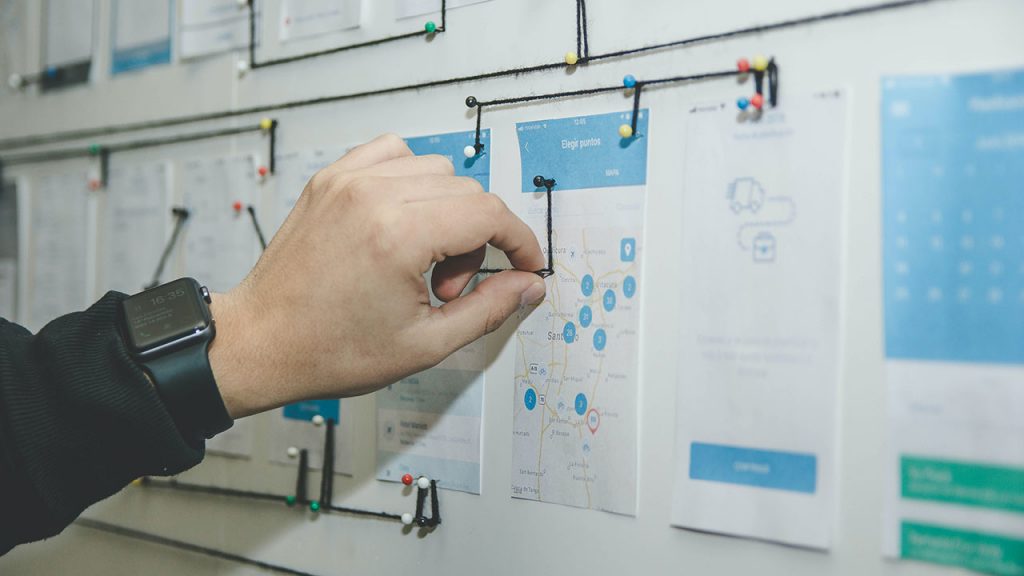 Person's hand adds pin to a noticeboard filled with printed paper charts