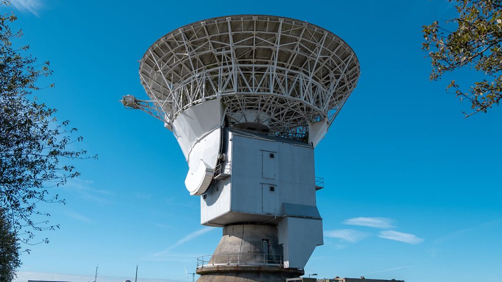 Large, white radar dish pointing skywards, blue sky background