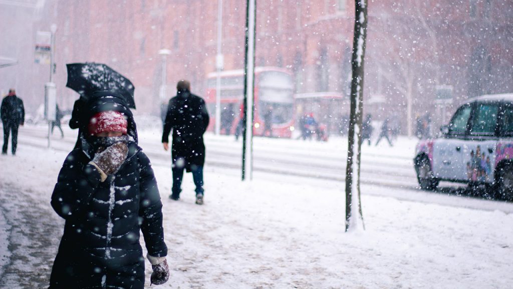 Pedestrians wearing warm coats walk through a blizzard on a snow covered pavement